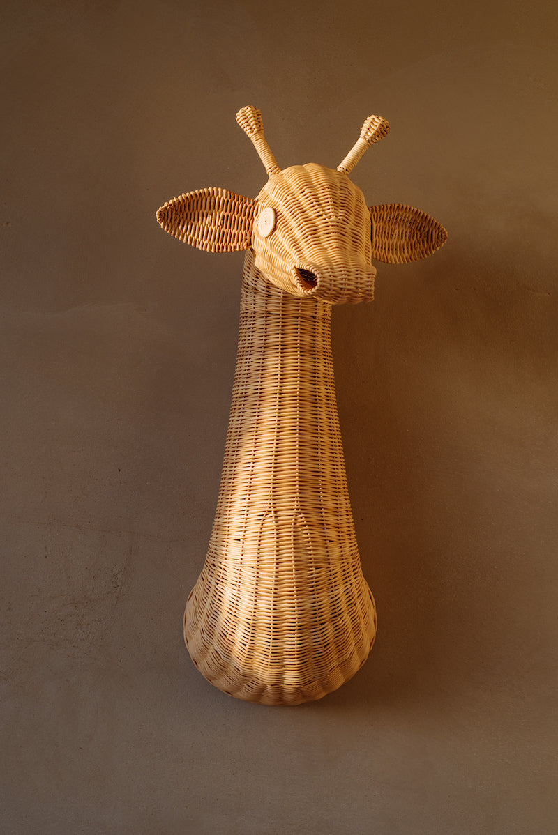 Op de afbeelding staat een schattig rotan giraffekop wanddecoratie, perfect voor de kinderkamer. Het organische ontwerp en de warme kleur van het rotan voegen een speels en natuurlijk element toe aan elke muur.