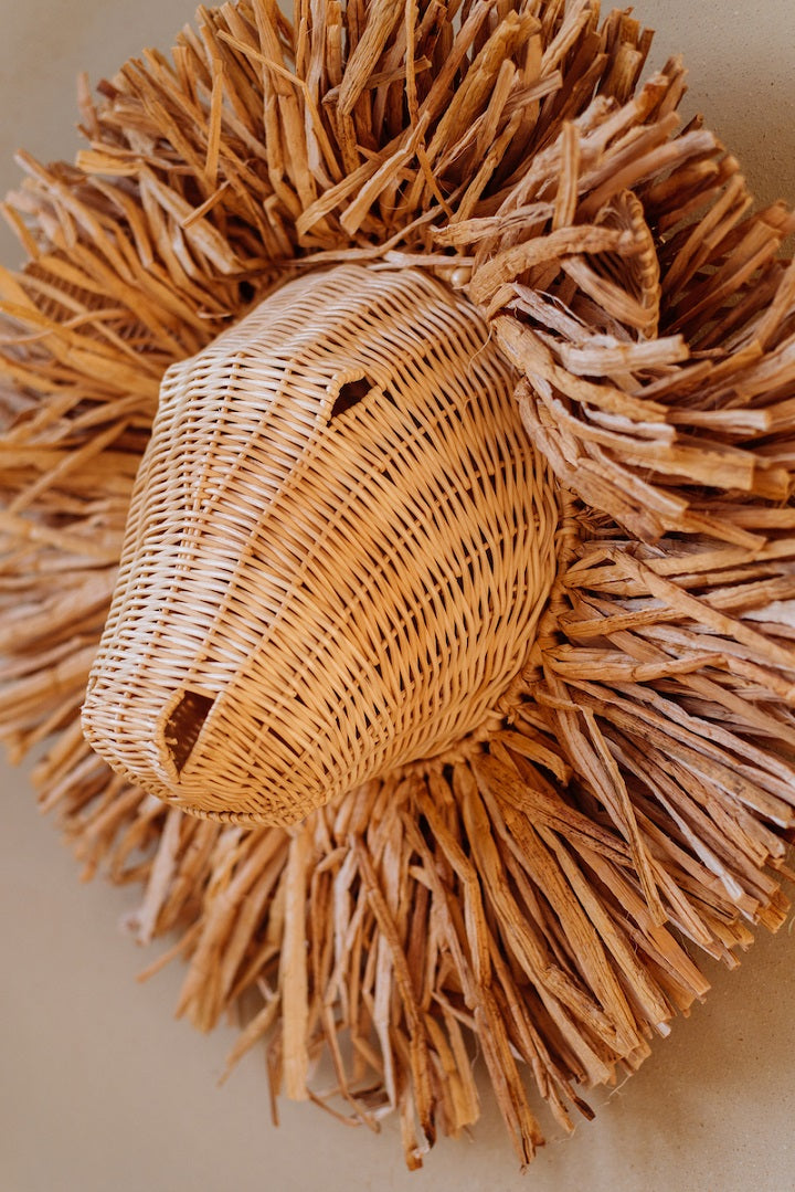 Op de afbeelding staat een charmante rotan leeuwenkop wanddecoratie voor de kinderkamer. Het organische ontwerp en de warme kleur van het rotan geven deze decoratie een unieke en betoverende uitstraling, perfect voor het creëren van een gezellige en speelse sfeer.